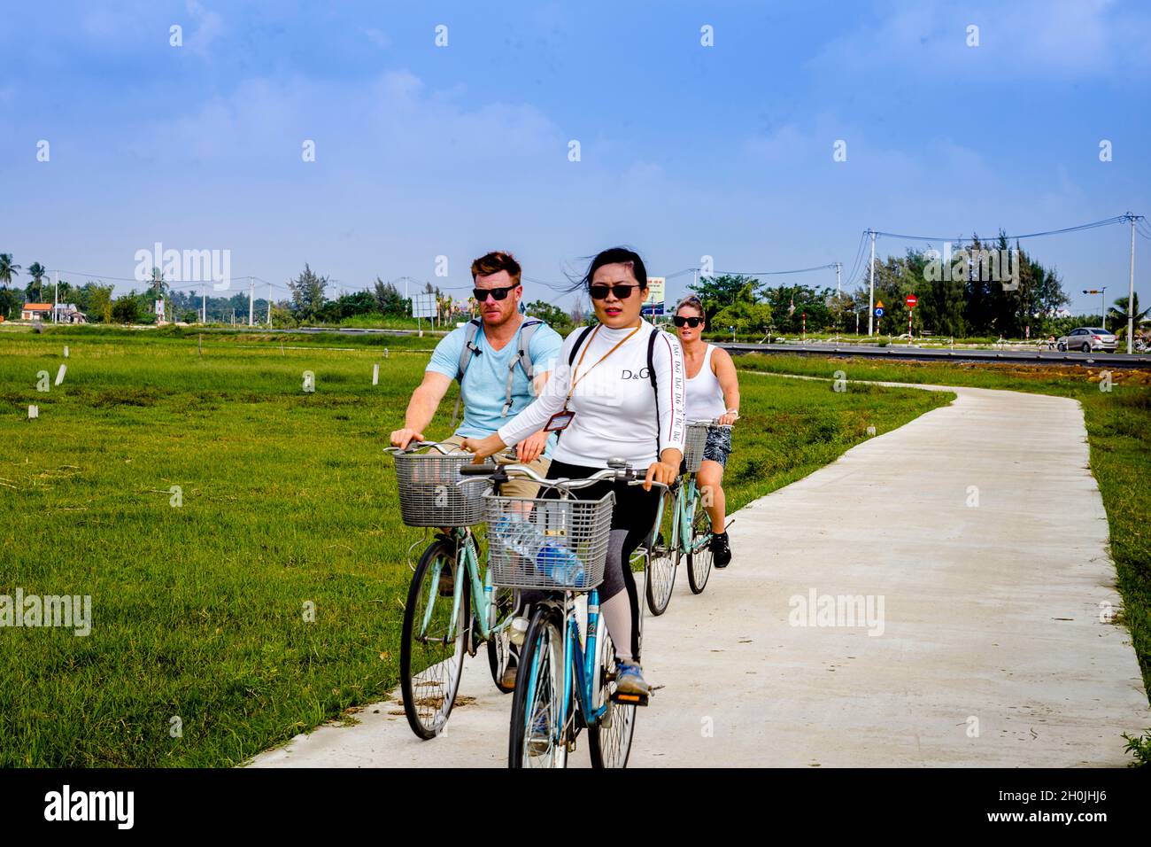 Tre ciclisti attraversano i campi di riso di Hoi An. Foto Stock