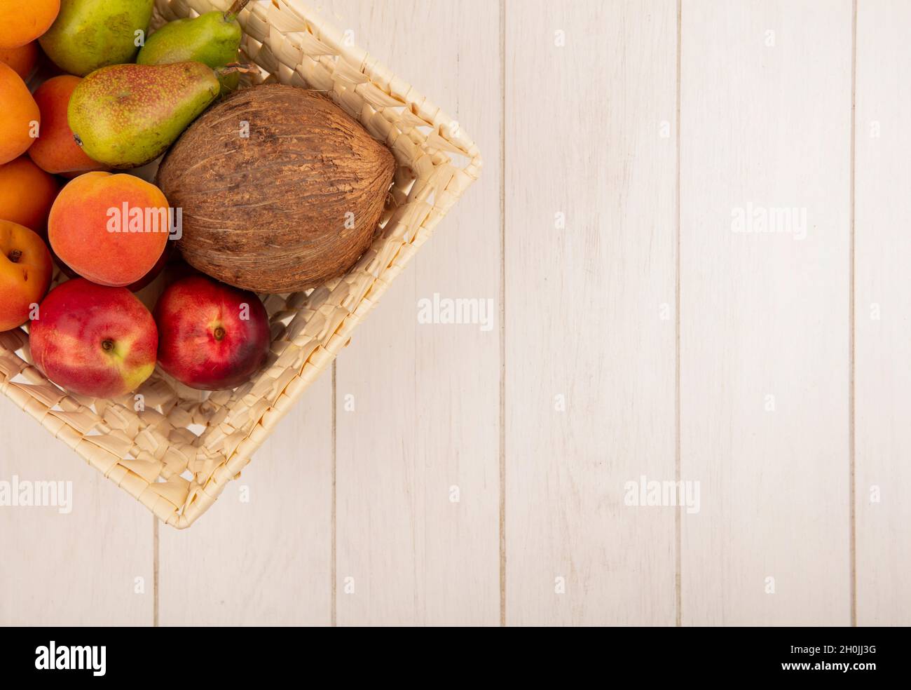 vista dall'alto di frutta come pera di pesca al cocco in cestino con foglie su sfondo di legno con spazio copia Foto Stock