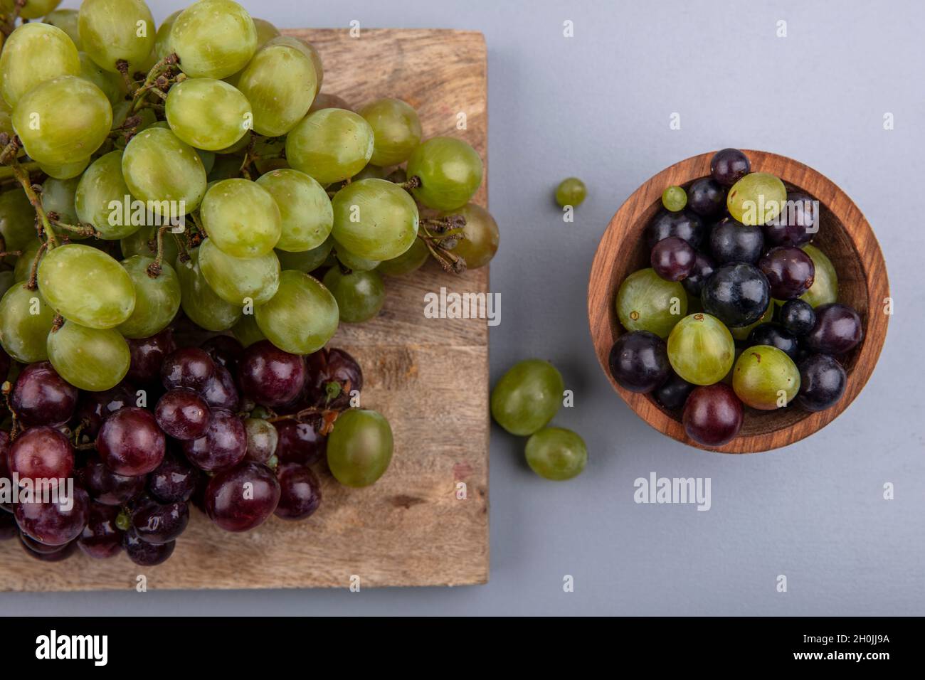 vista dall'alto delle uve bianche e rosse sul tagliere e ciotola di acini su sfondo grigio Foto Stock