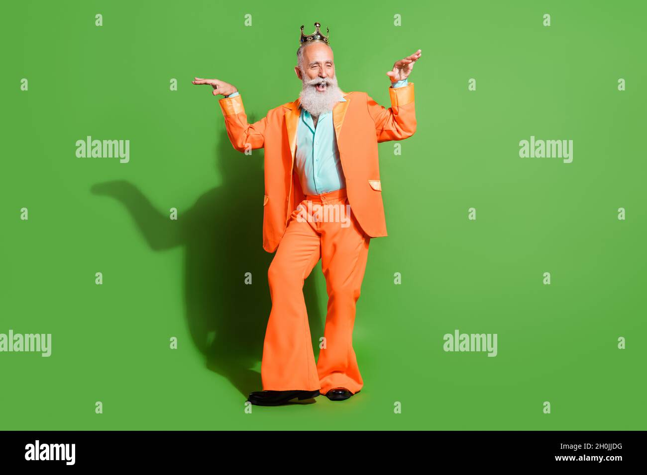 Vista a tutta lunghezza del corpo di attraente allegro nonno funky ballare indossando corona isolato su sfondo di colore verde brillante Foto Stock