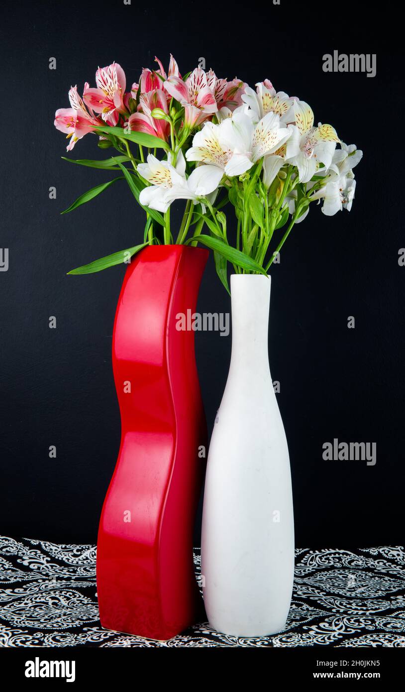 vista laterale di fiori di alstroemeria bianchi e rosa su sfondo nero in vasi bianchi e rossi Foto Stock