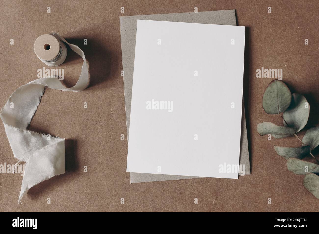 Matrimonio naturale, cancelleria di compleanno. Biglietto d'auguri vuoto, mockup di invito con busta artigianale e ramo di eucalipto secco. Carta grunge beige Foto Stock