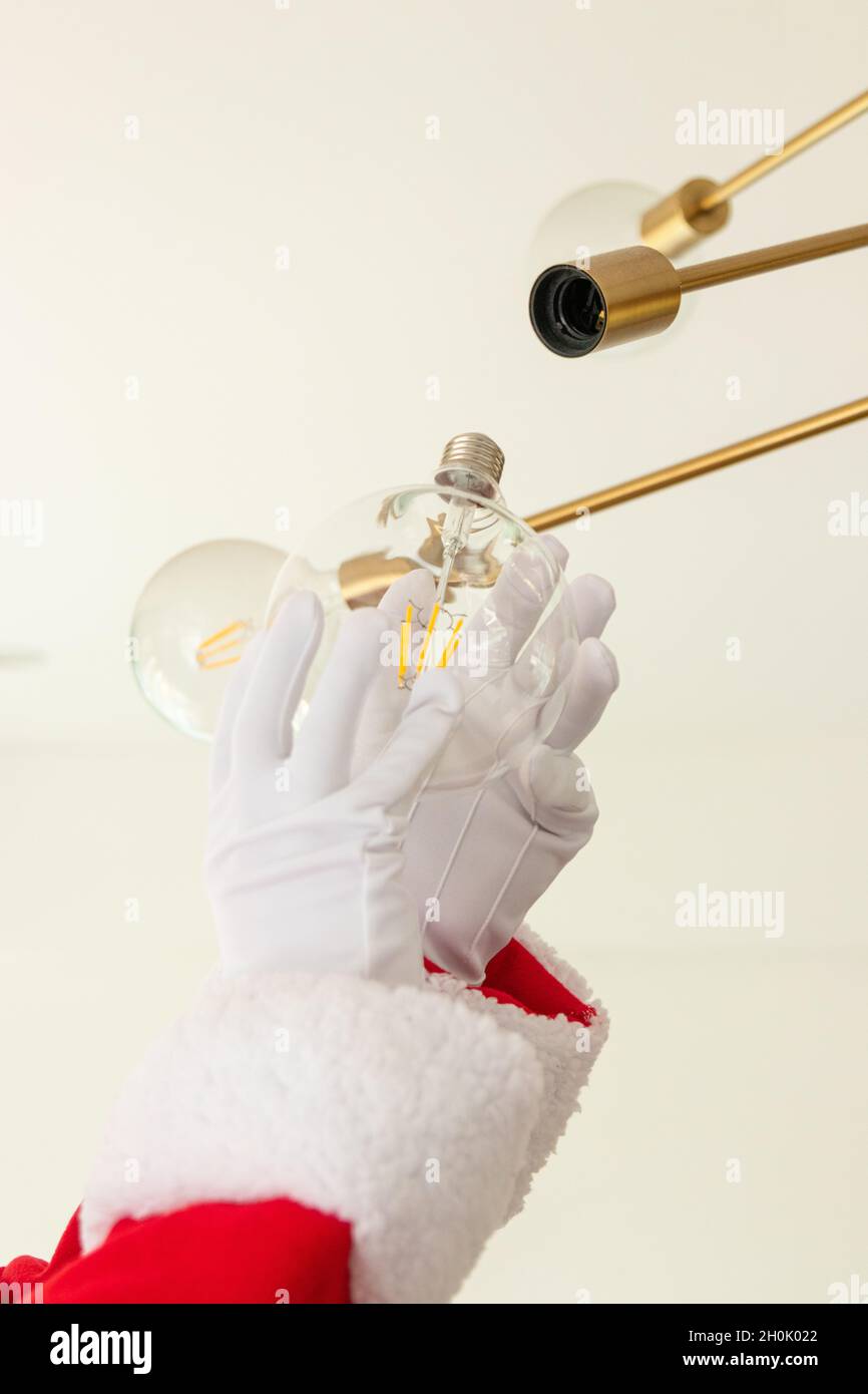 Babbo Natale sta cambiando una lampadina nel soggiorno di una casa Foto Stock