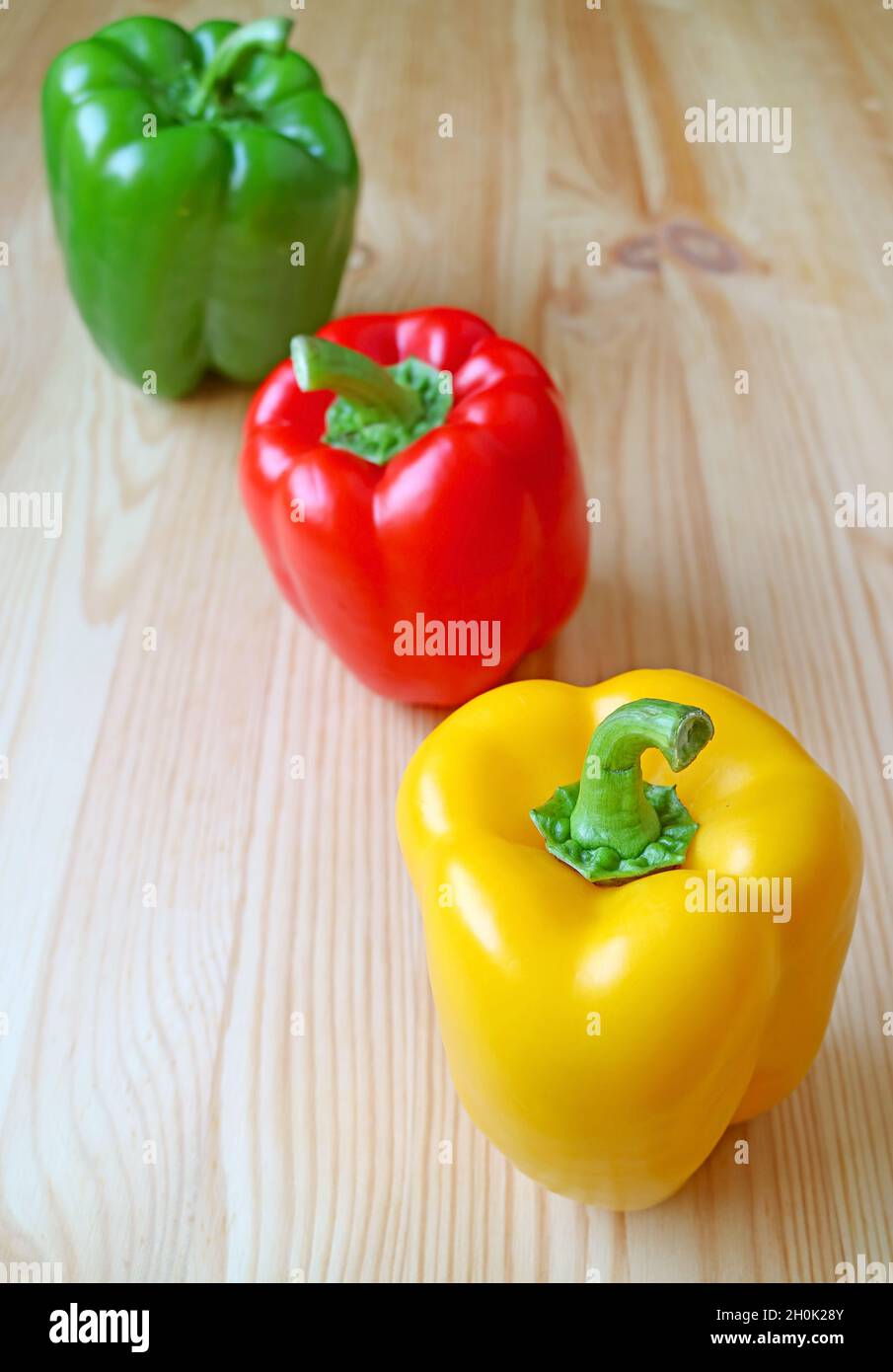 Peperoni tricolore allineati su sfondo di legno marrone chiaro Foto Stock