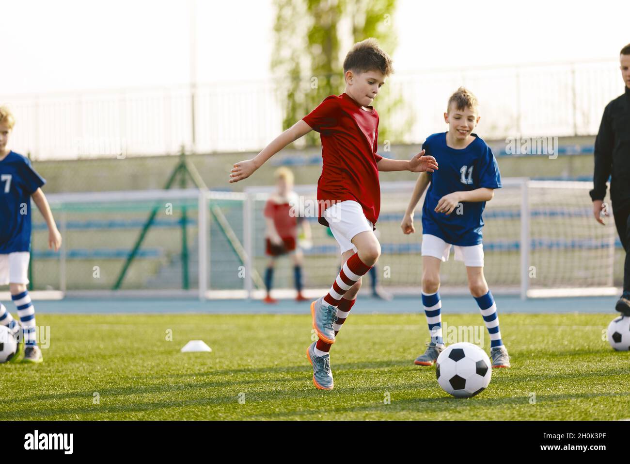 Giovani atleti Junior in maglia da calcio rossa e blu. Due ragazzi gareggiano per la palla. Educazione sportiva. Bambini giocatori di calcio Kicking Ball su Soccer Fie Foto Stock