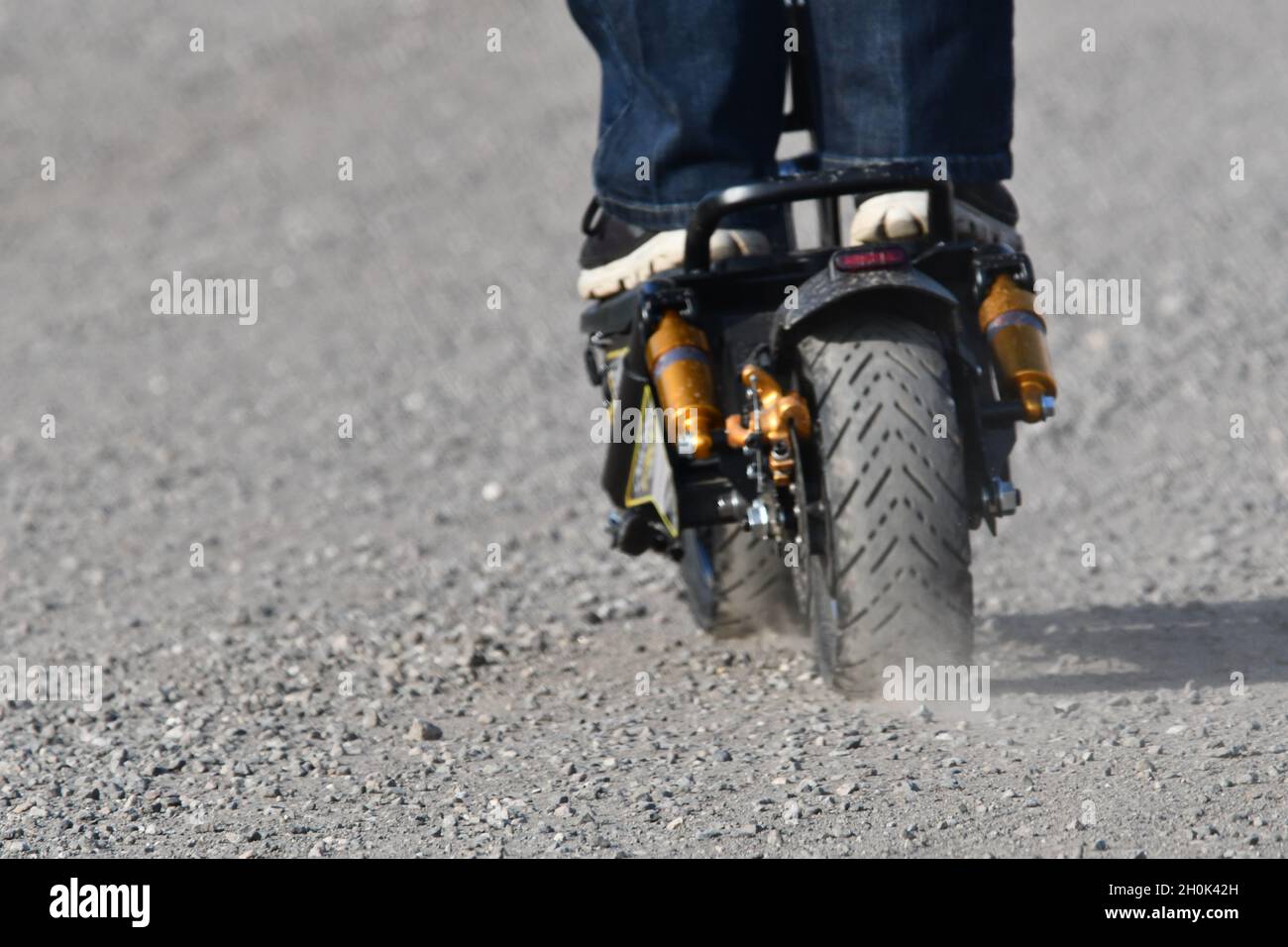 Vista posteriore di un e-scooter in movimento che calcia lo sporco Foto Stock