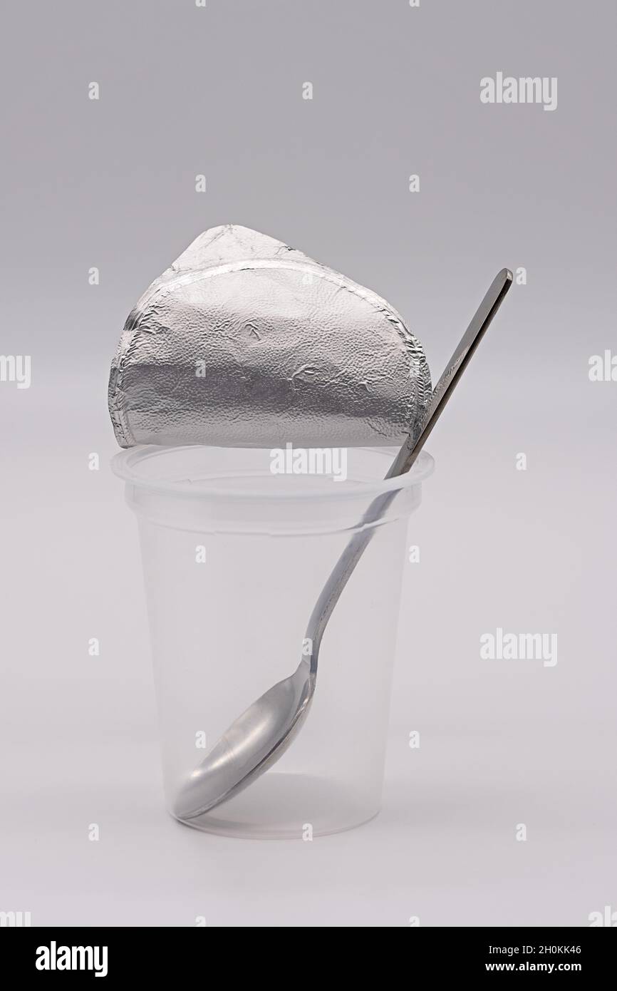 tazza per yogurt vuota e trasparente con lamina di alluminio aperta e cucchiaio in acciaio inox isolato su sfondo bianco Foto Stock