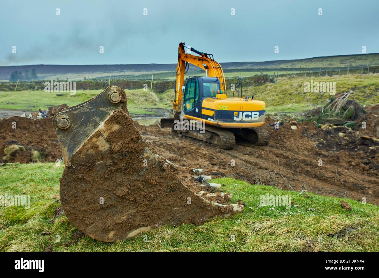 Una benna grande attende di essere usato come un scavatore JCB inizia a liberare una cava e una punta disutilizzati Foto Stock