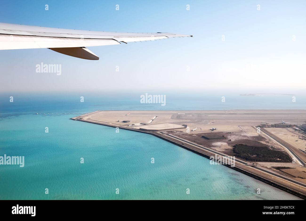 Ala di un aereo sopra il mare e un aeroporto, concetto di industria dei trasporti. Foto Stock