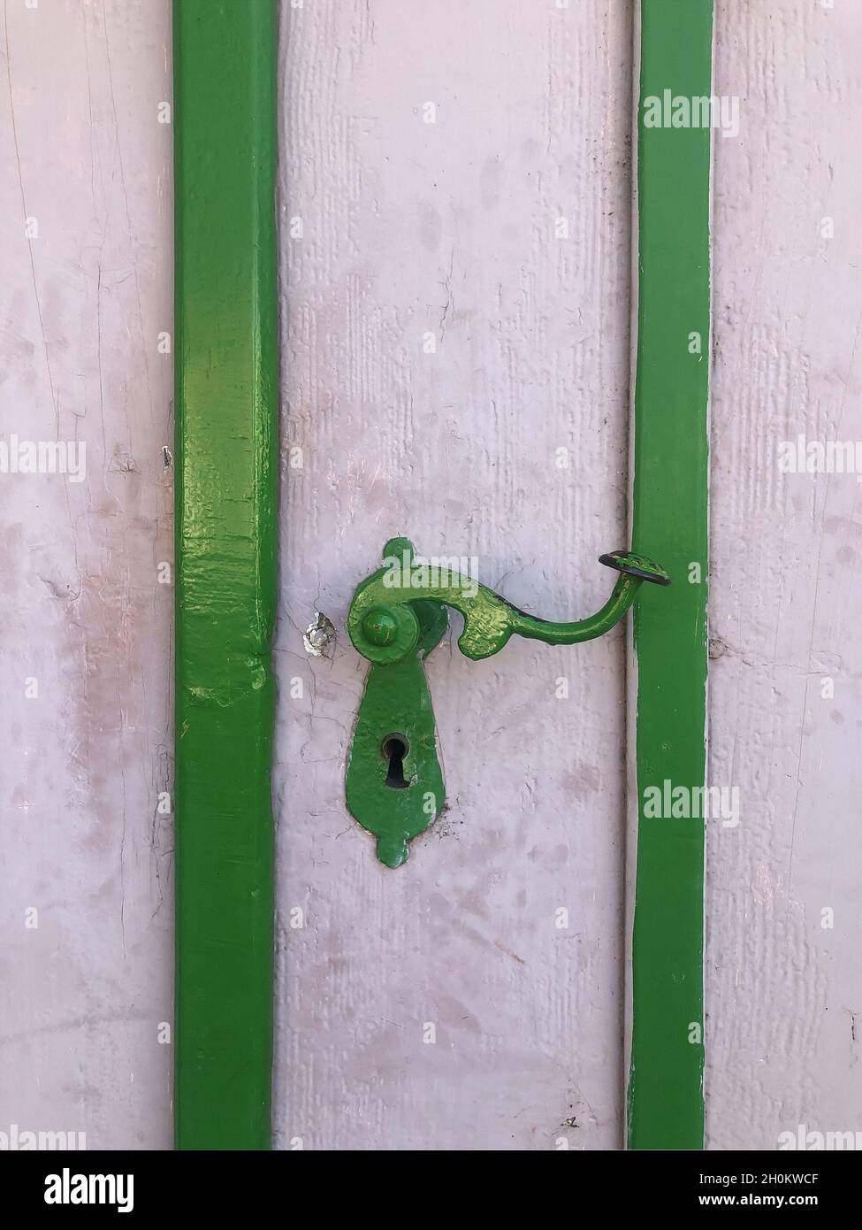 Primo piano di una porta dipinta di bianco con una vecchia maniglia metallica dipinta di verde Foto Stock