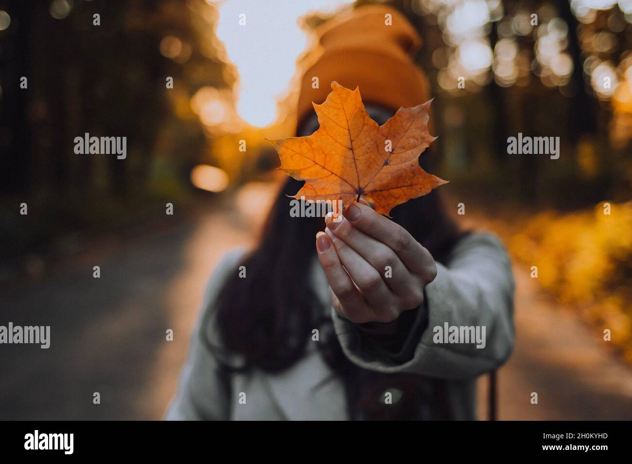 La giovane donna tiene una foglia di acero davanti al suo volto coprendola Foto Stock