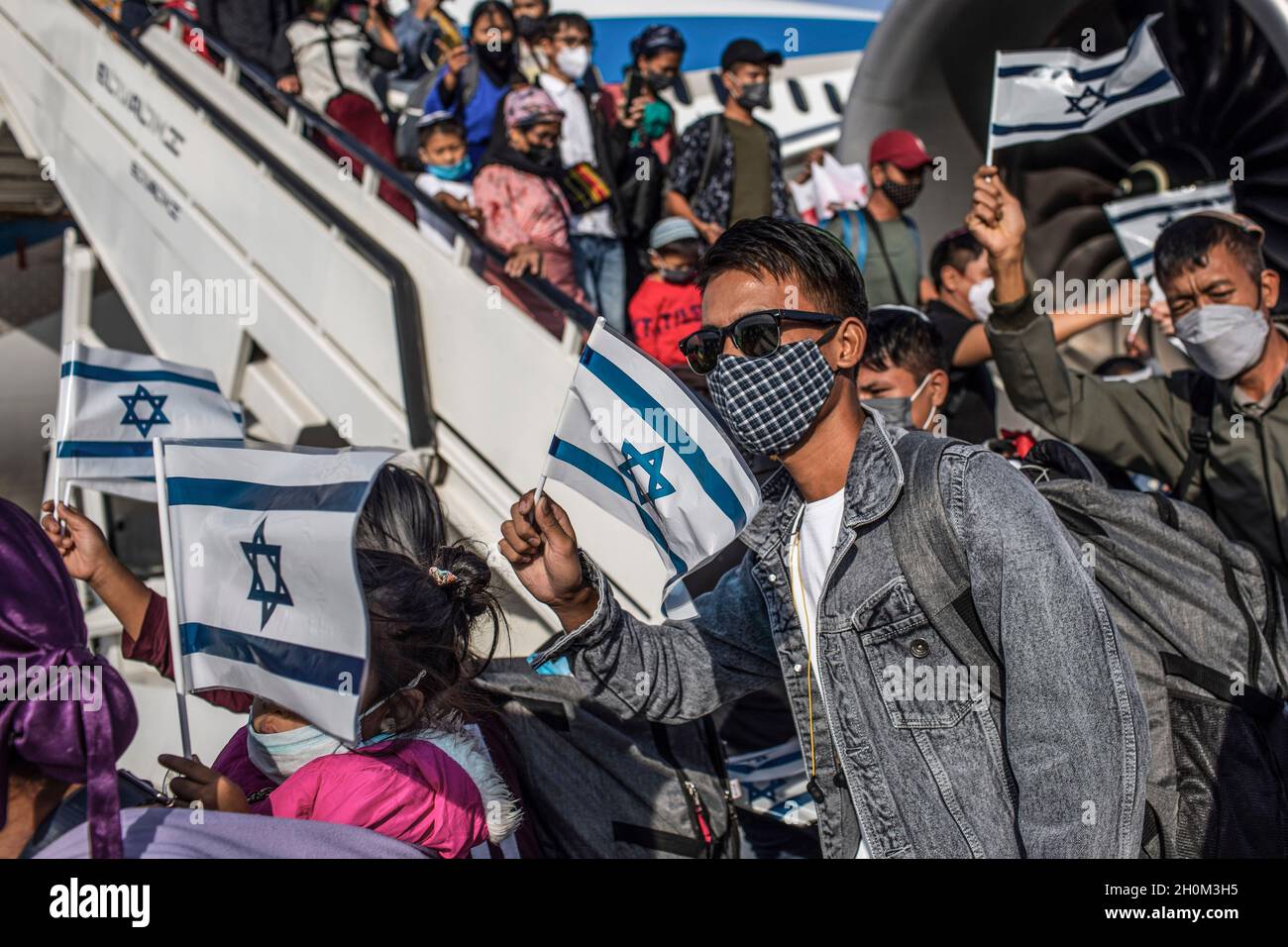 Tel Aviv, Israele. 13 ottobre 2021. I nuovi emigranti ebrei della comunità Bnei Menashe (figli di Manasseh) in India, detengono bandiere israeliane mentre acclamano all'arrivo all'Aeroporto ben Gurion vicino a Tel-aviv. 250 emigranti della comunità di Bnei Menashe, che sostenevano di essere una delle dieci tribù perdute d'Israele che si stabilirono in India, sono arrivati oggi in Israele come parte di un'operazione del Ministero di Aliyah e integrazione (assorbimento degli immigrati). Credit: Ilia Yefimovich/dpa/Alamy Live News Foto Stock