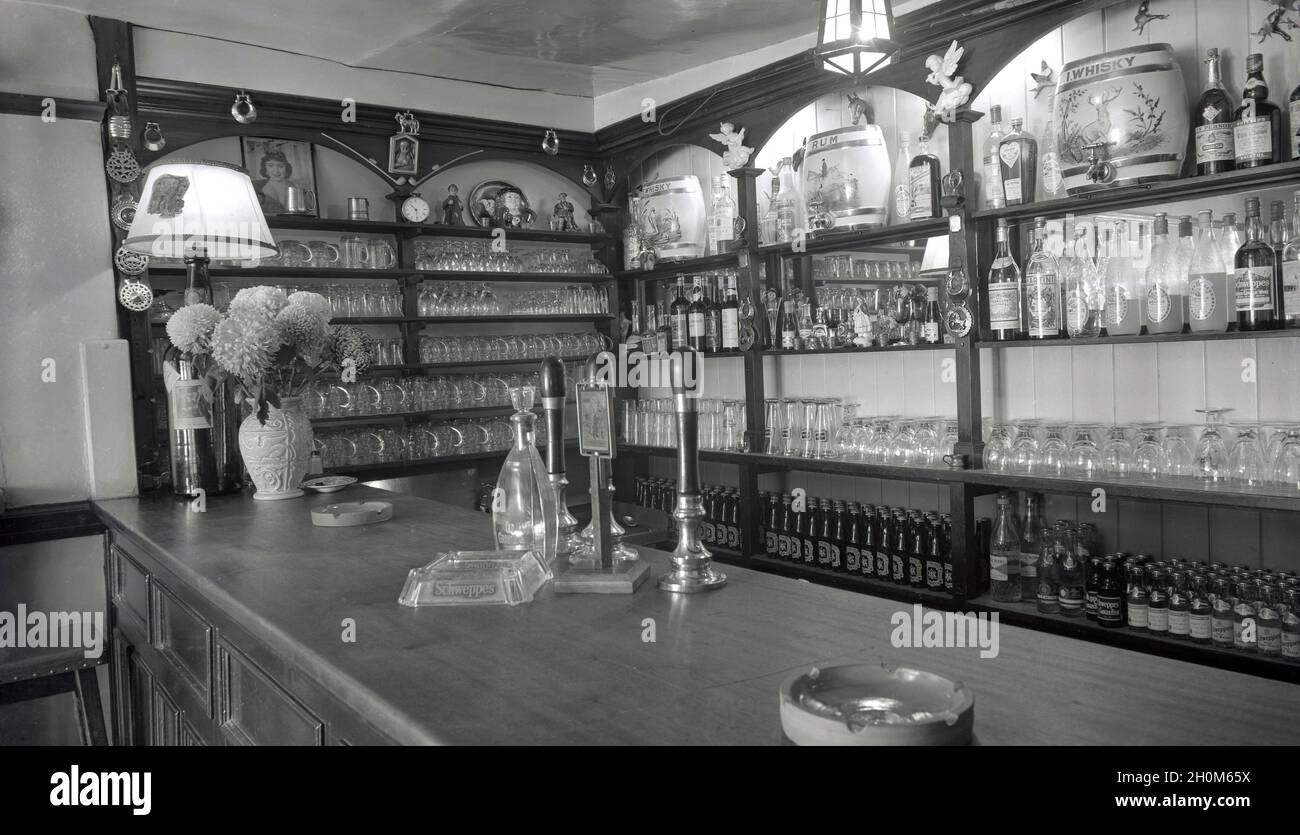 1950, storico, pub bar presso l'Angel Inn, Witney, Oxford, Inghilterra, Regno Unito, mostra vere e proprie pompe a mano e posacenere sul bancone e dietro, bottiglie di birra, tankard di vetro e bottiglie di liquori. Foto Stock