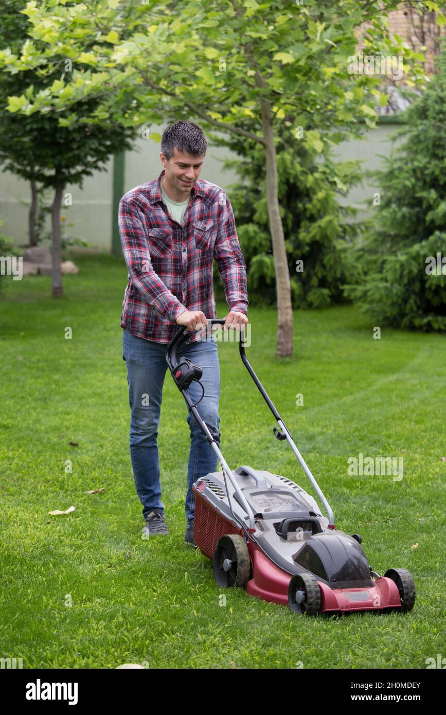Bel giovane uomo che tagliano l'erba con il rasaerba elettrico in cortile in primavera Foto Stock