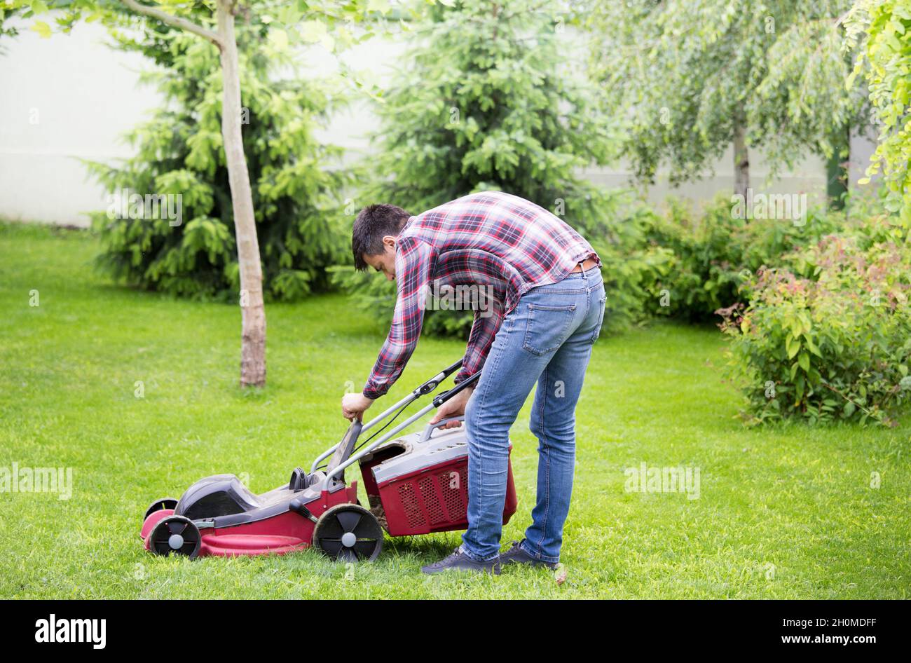 Bel giovane uomo che tagliano l'erba con il rasaerba elettrico in cortile in primavera Foto Stock