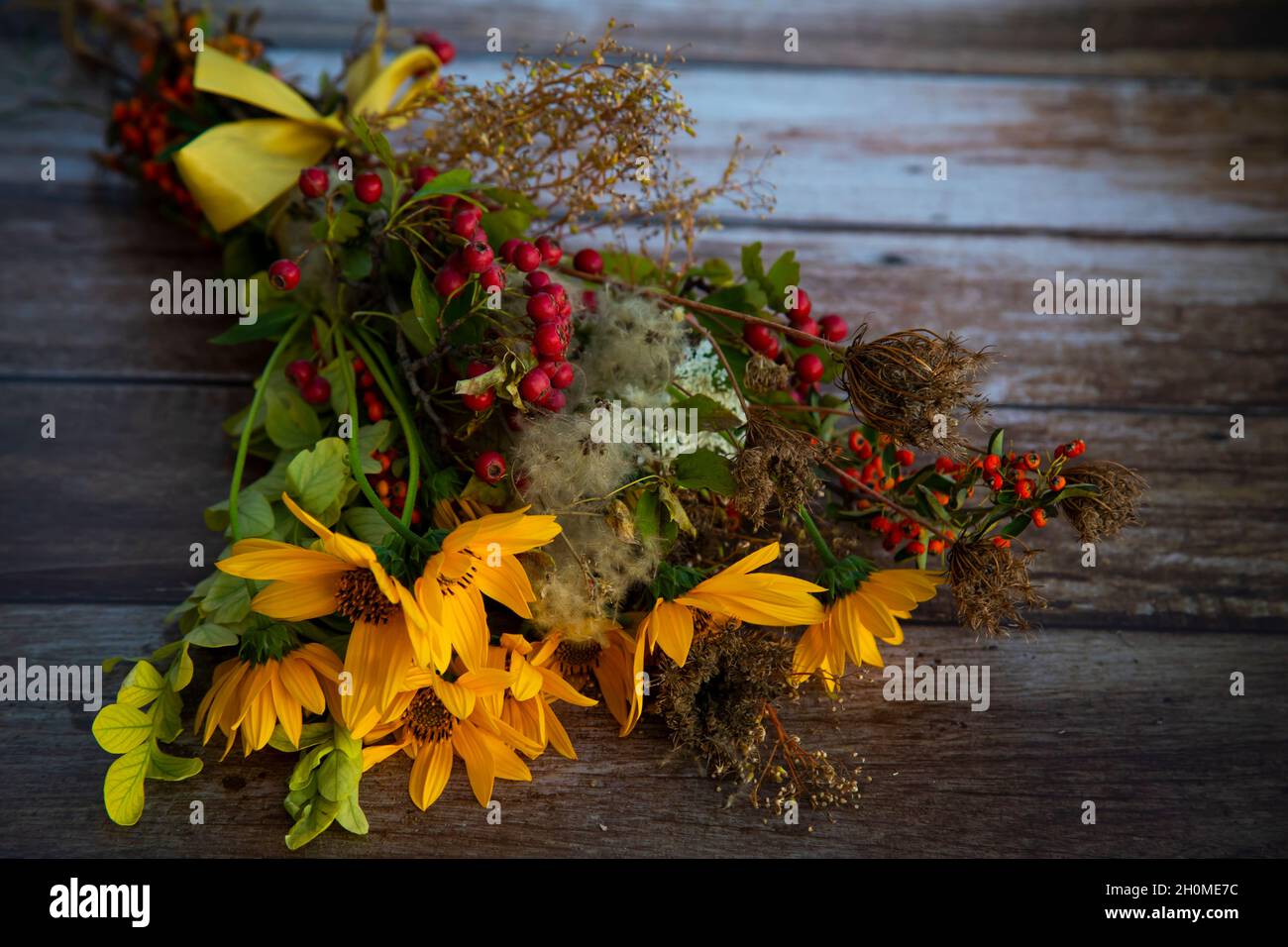 bouquet autunnale raccolto da fiori gialli, bacche selvatiche e piante secche su un tavolo di legno Foto Stock