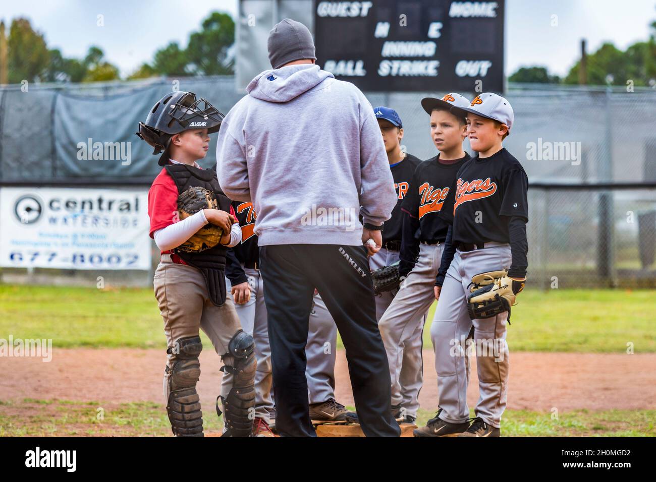 Allenatore che parla con giovani maschi pre-teen al tumulo di caraffa mentre gioca a baseball in uniforme Foto Stock