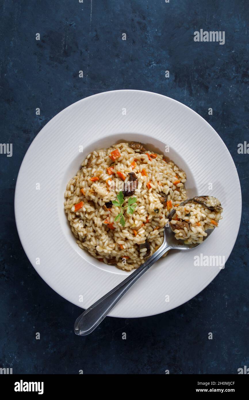 Risotto, riso italiano con funghi, verdure e prezzemolo servito su piatto di porcellana bianca Foto Stock