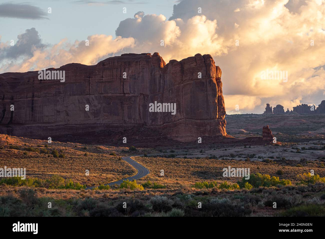 Tortuosa strada panoramica attraverso il bellissimo paesaggio desertico al tramonto dell'ora d'oro con nuvole e formazioni rocciose puffy, Arches National Park, Utah Foto Stock