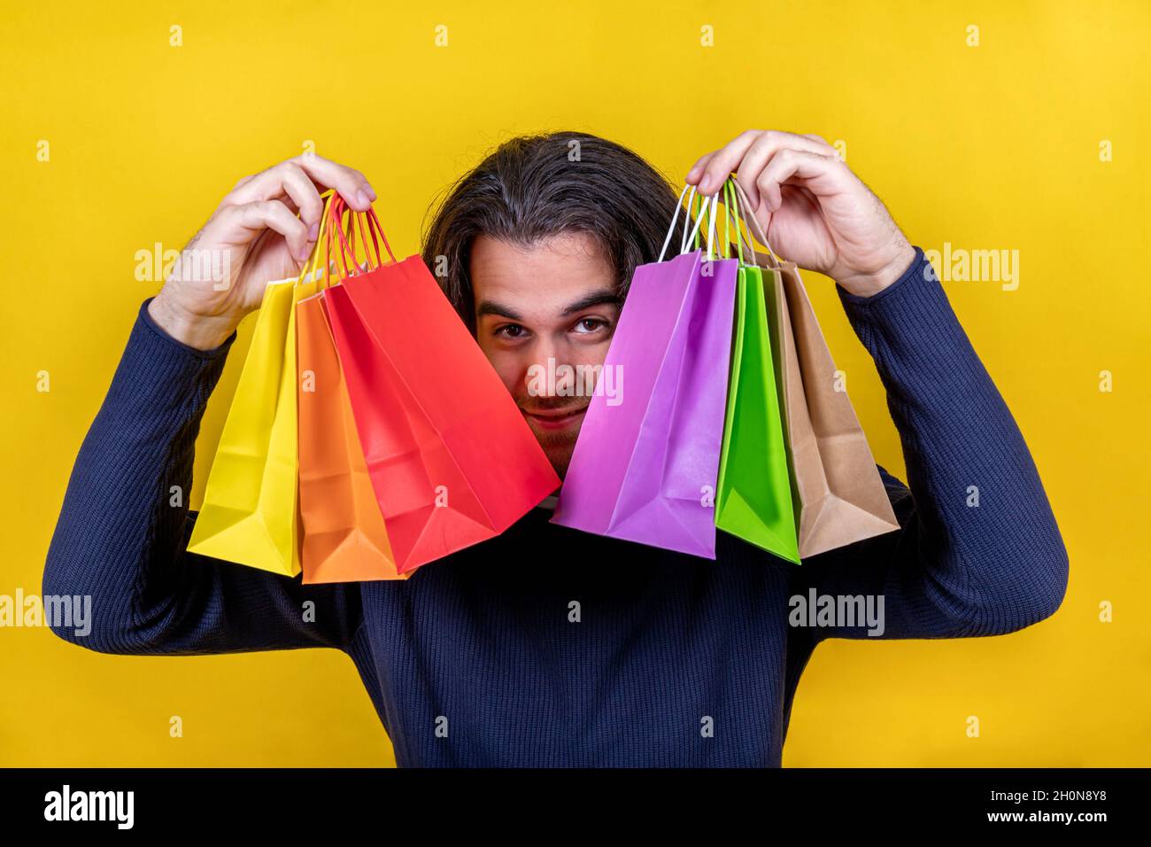 Sorpresa! Giovane uomo su sfondo giallo brillante che mostra diversi sacchetti di carta colorati con un aspetto allettante. Shopping e regali. Foto Stock