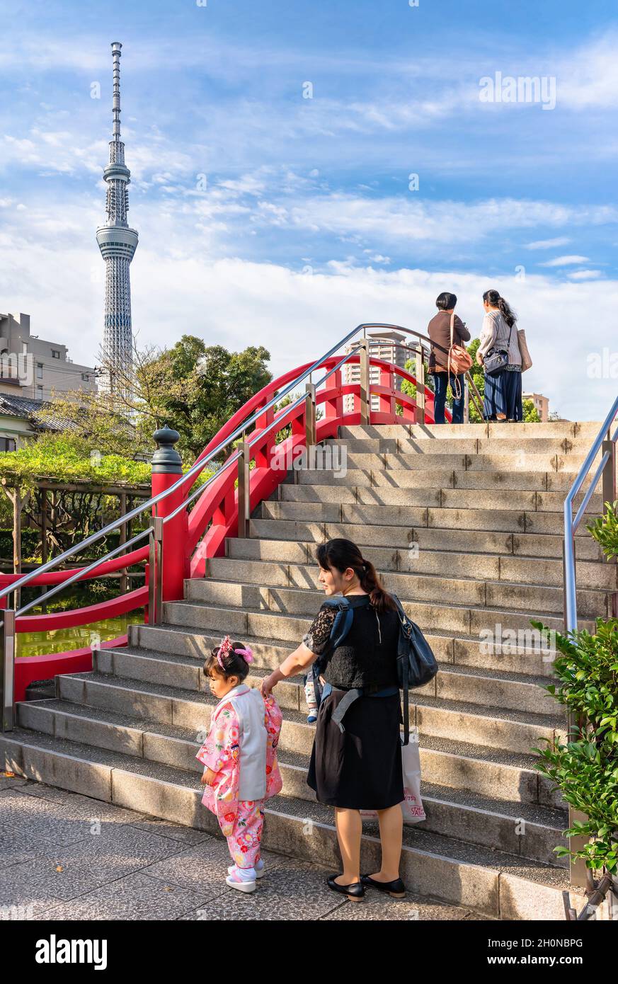 tokyo, giappone - ottobre 26 2019: Bambina in kimono con sua madre ai piedi delle scale del tradizionale ponte rosso taikobashi sovrastato da Skytree Foto Stock