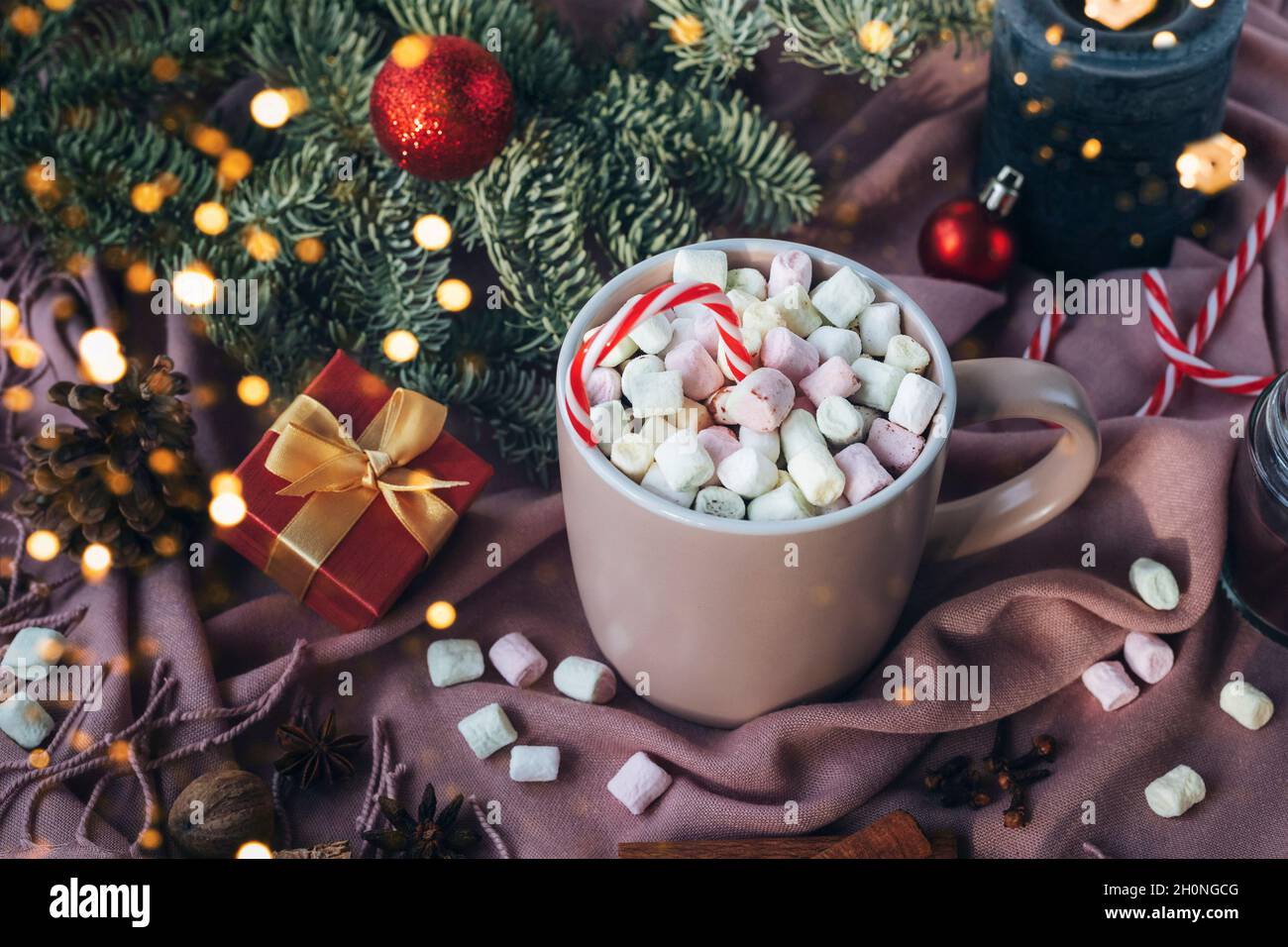 Tazza di cacao con marshmallow, rami di abete, luci di Natale e regalo in una scatola su sfondo tessile rosa. Natale, concetto di vacanze invernali. Vista dall'alto Foto Stock
