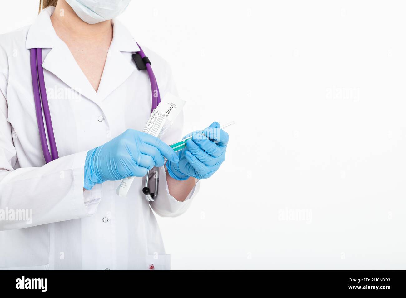 Un giovane infermiere in una maschera apre una siringa su sfondo bianco in un cappotto bianco, per fare una vaccinazione, un'iniezione. Il concetto di vaccinazione e. Foto Stock