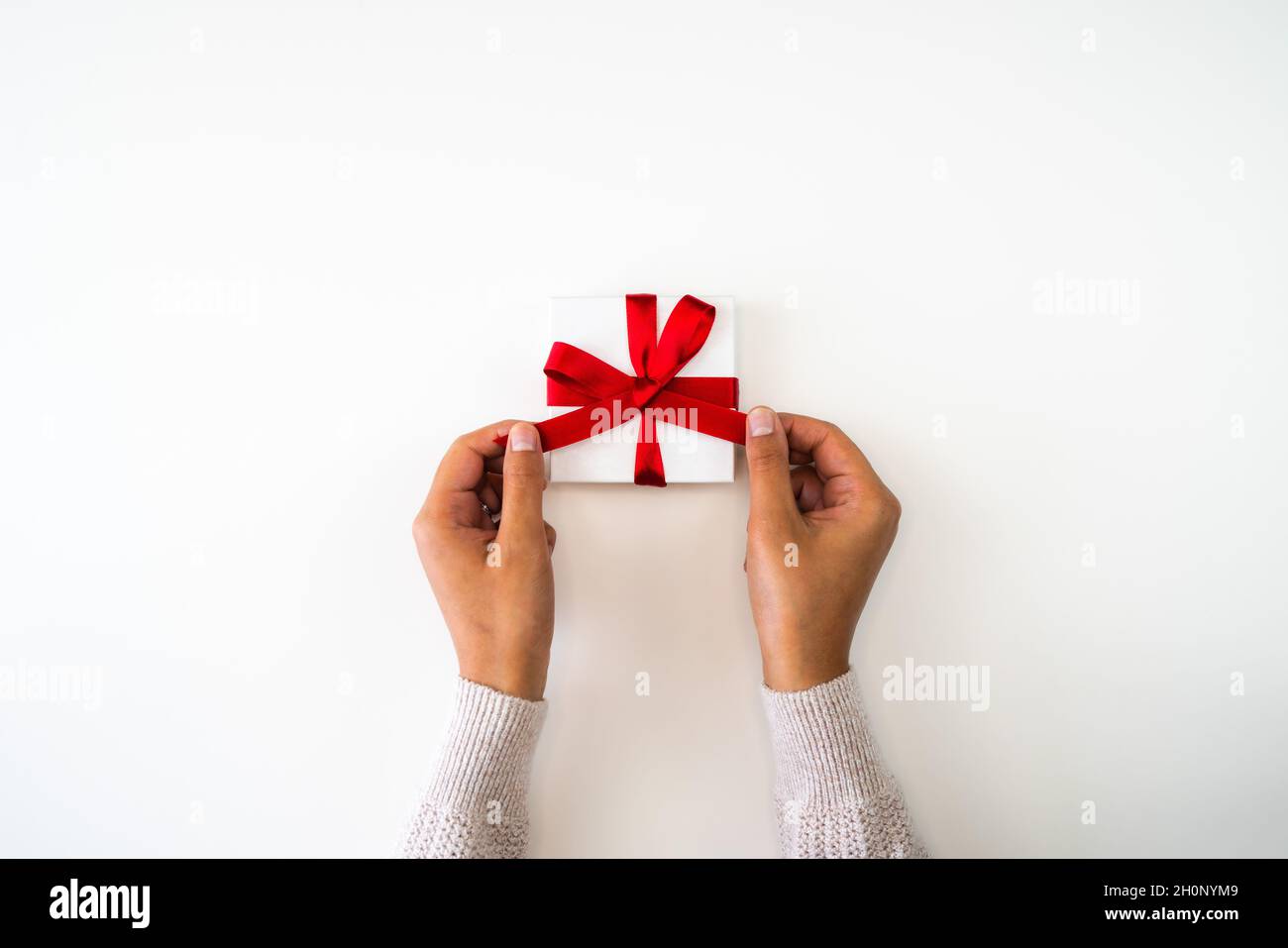 Sfondo di vacanza o Natale o immagine di sfondo primo piano di mani da una razza mista afroamericana donna indossando un maglione che lega un arco a nastro rosso Foto Stock