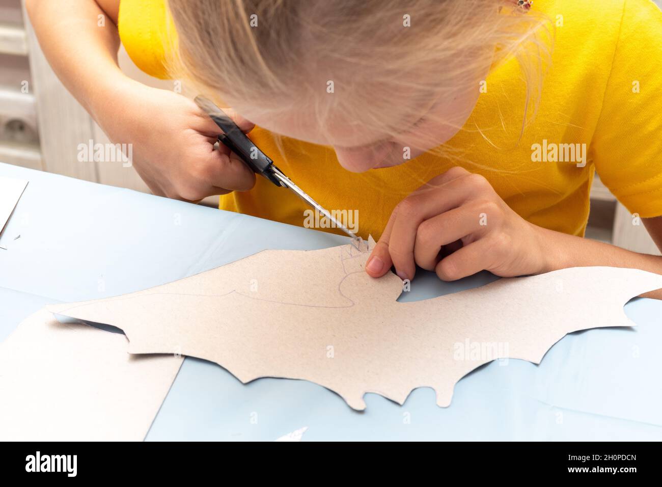 Una ragazza taglia una decorazione di Halloween a casa da carta nera. Fai da te artigianato decorazioni per la casa. Il bambino fa i mestieri di carta, origami Foto Stock