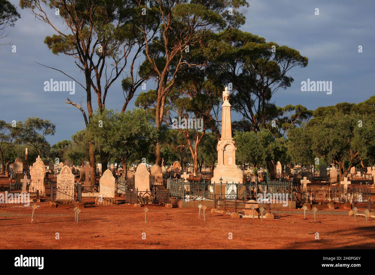 Cimitero di Kalgoorlie con terra rossa, lapidi, alberi e nuvole scure subito dopo una tempesta di tuore a Kalgoorlie, Australia Occidentale Foto Stock