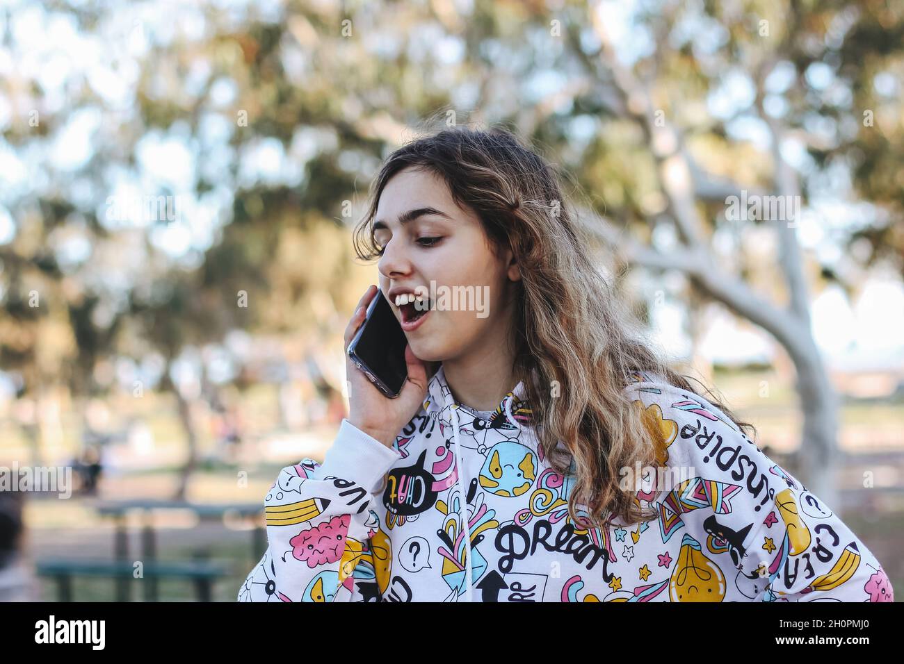 Ragazza adolescente carina che parla con gli amici per telefono. Abbastanza teen fuori agli alberi Foto Stock