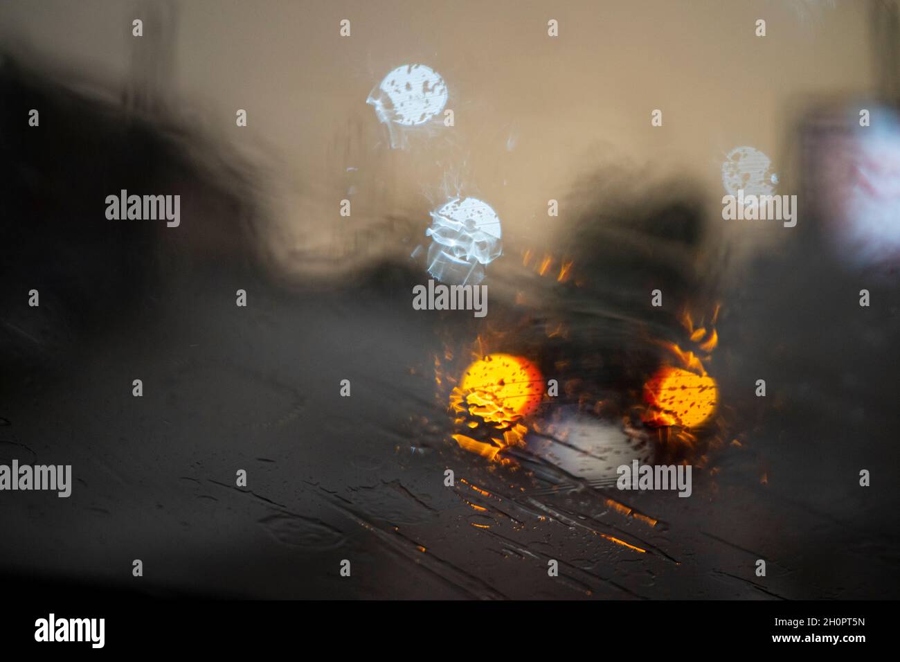 Tempo piovoso, pioggia attraverso il vetro, sfondo astratto dalla luce di automobili e semafori, sfocato Foto Stock