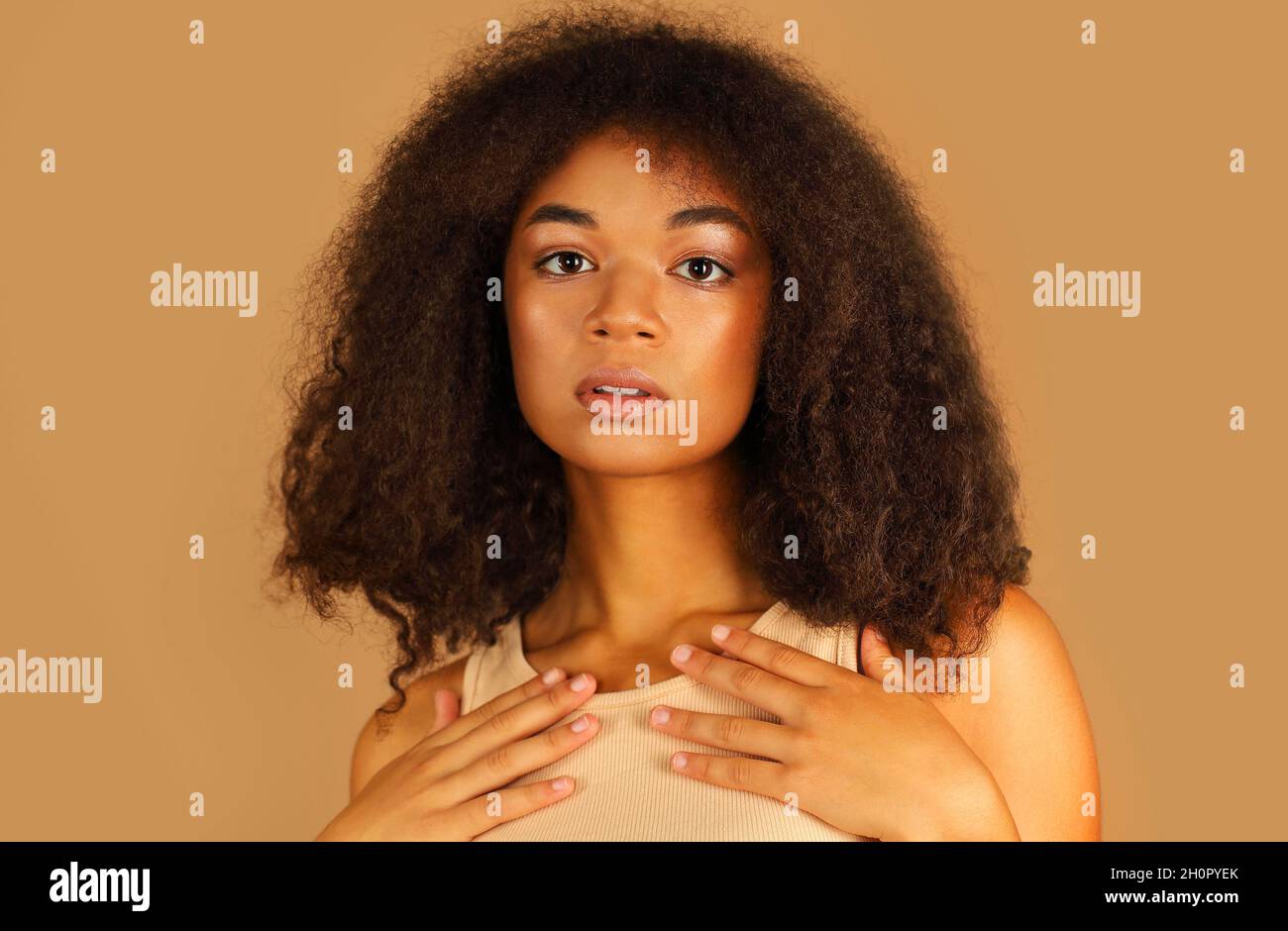 Primo piano ritratto di razza mista giovane ragazza guardando la fotocamera con tranquilla espressione del viso interrogante, tenendo le mani vicino al collo in piedi isolato ov Foto Stock