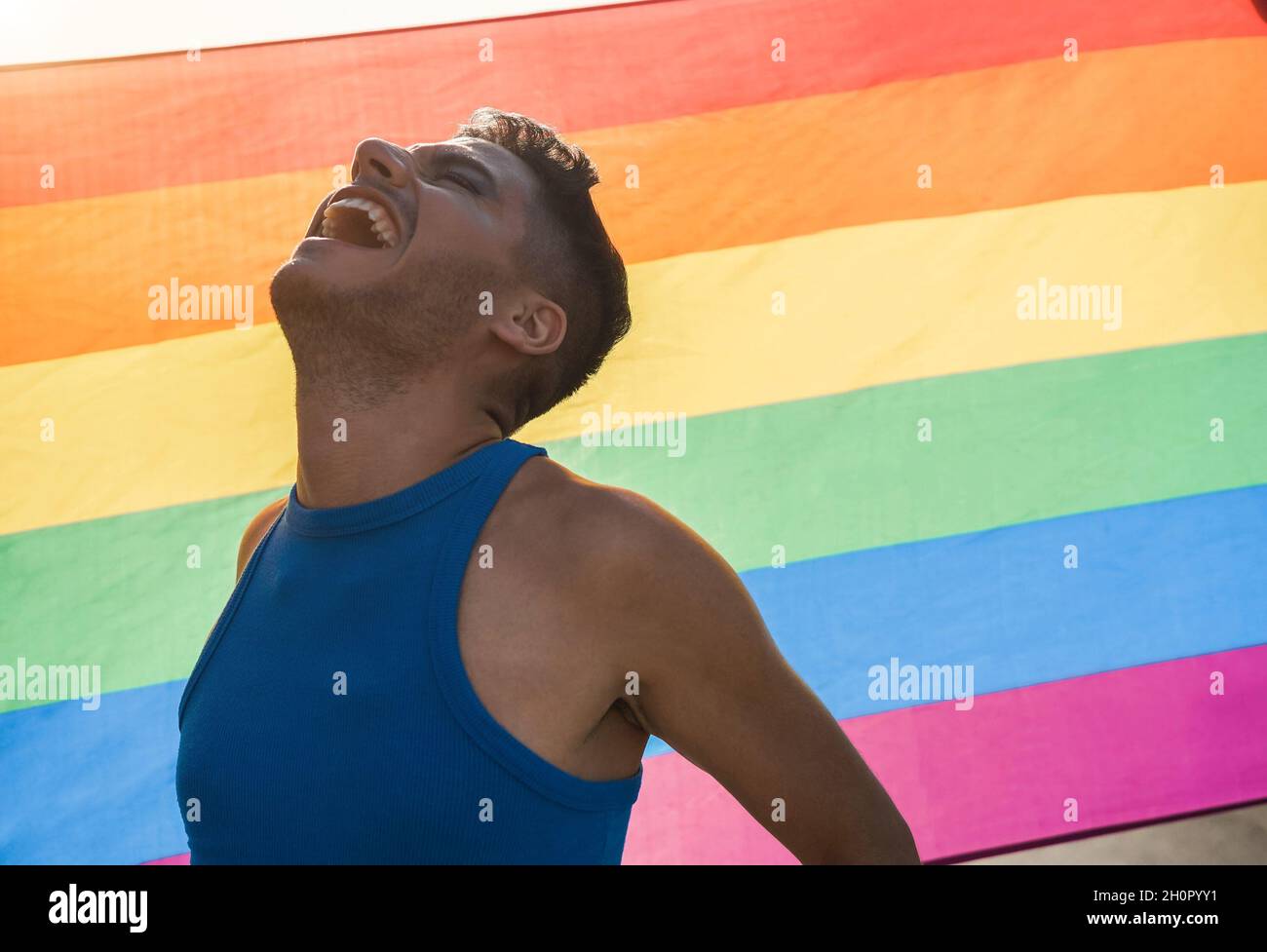 Giovane uomo transgender con trucco sorridente con bandiera arcobaleno lgbt sullo sfondo Foto Stock