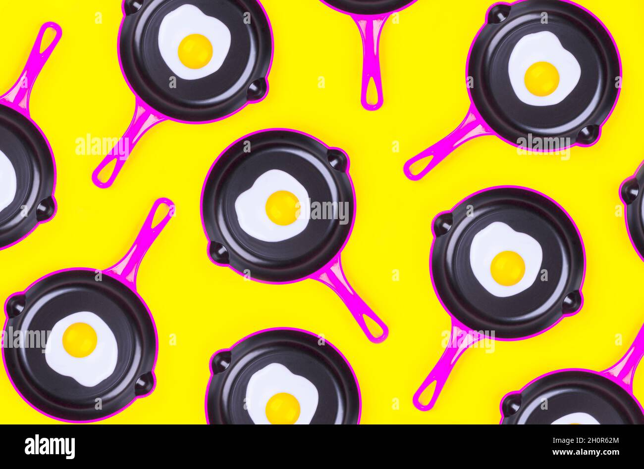 Motivi creativi con uova fritte su padelle rosa su sfondo giallo. Vista dall'alto. Modello creativo in stile minimal. Disposizione piatta. Banner. Foto Stock