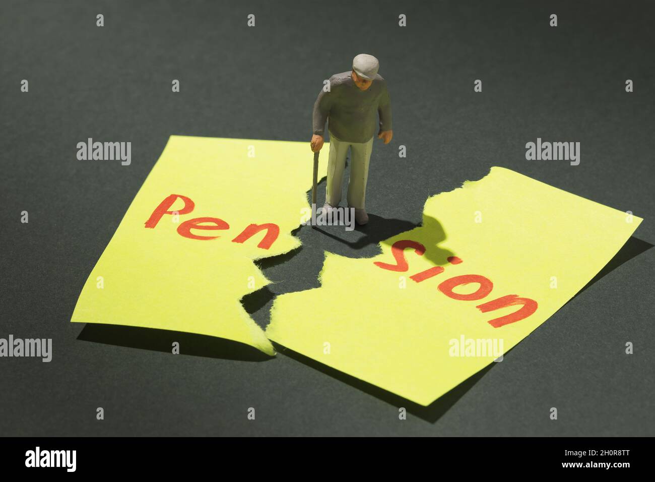 Uomo anziano con una crutch e un foglio strappato di carta con testo, concetto sul tema della non pensione in vecchiaia, giocattolo di plastica a forma di uomo Foto Stock