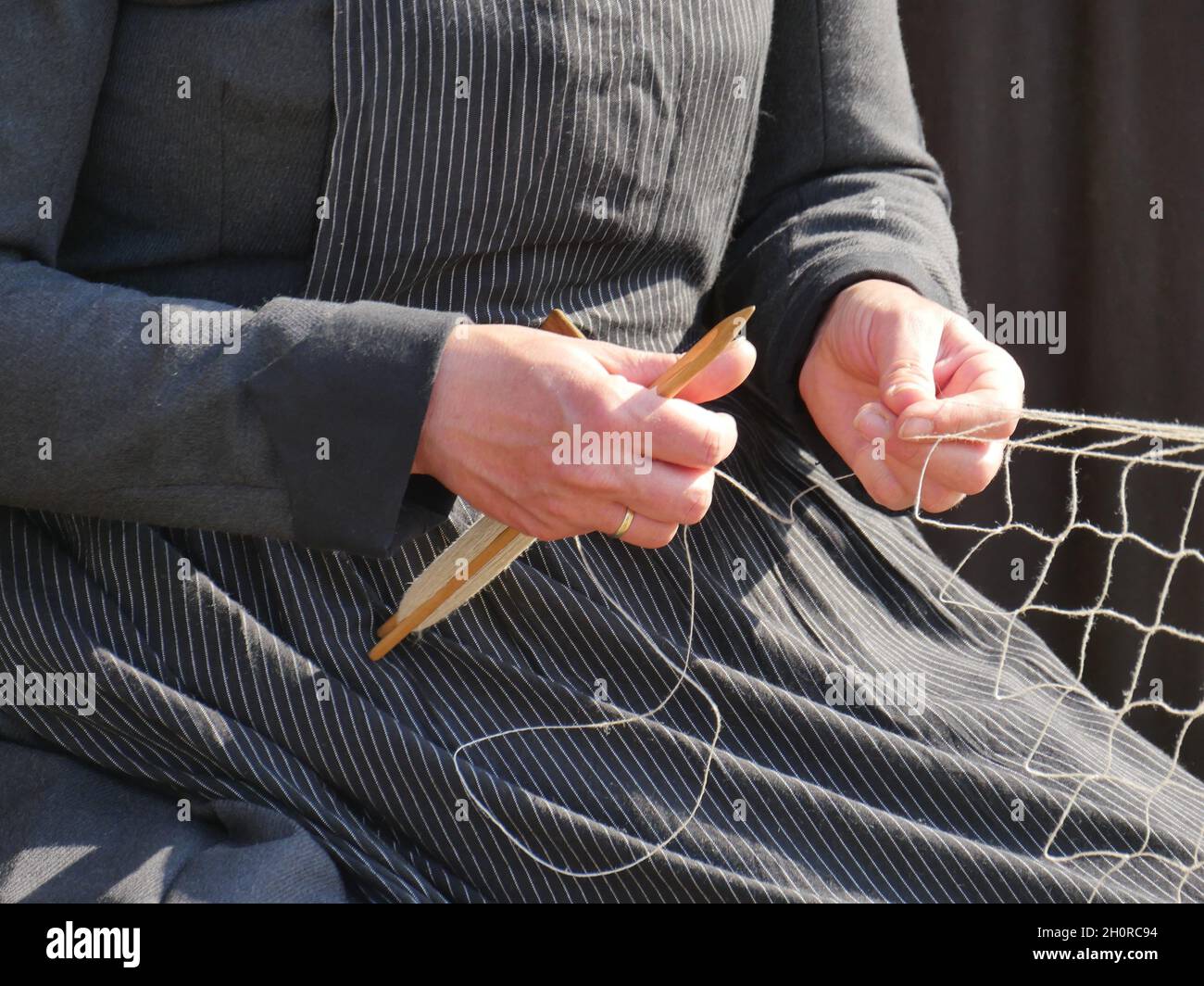 Le mani della moglie di un pescatore che tessono una nuova rete da pesca per il pesce, abbigliamento tradizionale, artigianato dei tempi passati Foto Stock