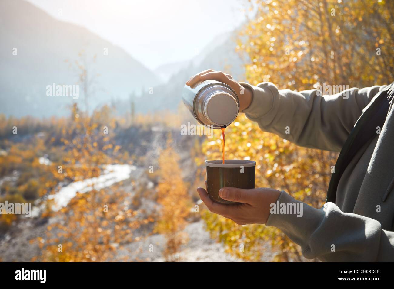 Donna turistica con thermos e tazza di caffè in autunno lago campeggio in montagna. Preparazione del caffè all'aperto Foto Stock