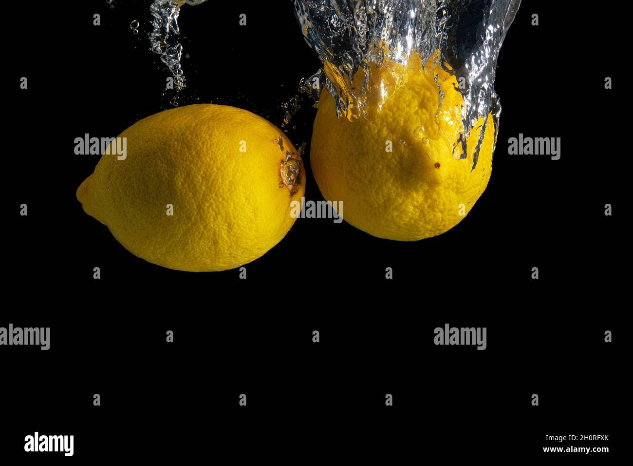 Limone giallo fresco in acqua spruzzata isolato su fondo nero. Concetto di cibo minimo. Foto Stock