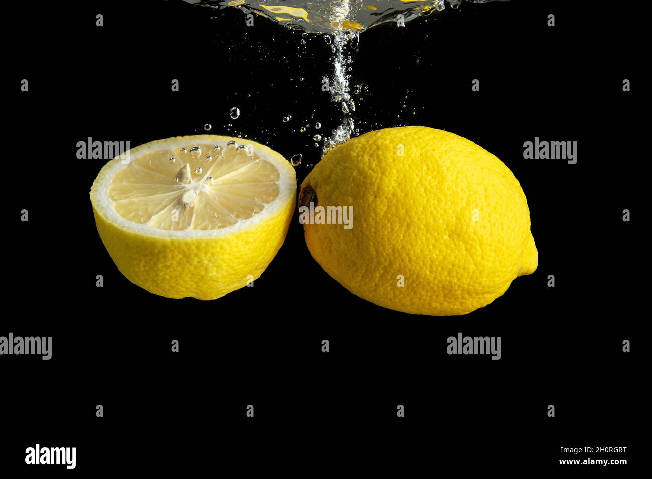 Limone giallo fresco in acqua spruzzata isolato su fondo nero. Concetto di cibo minimo. Foto Stock