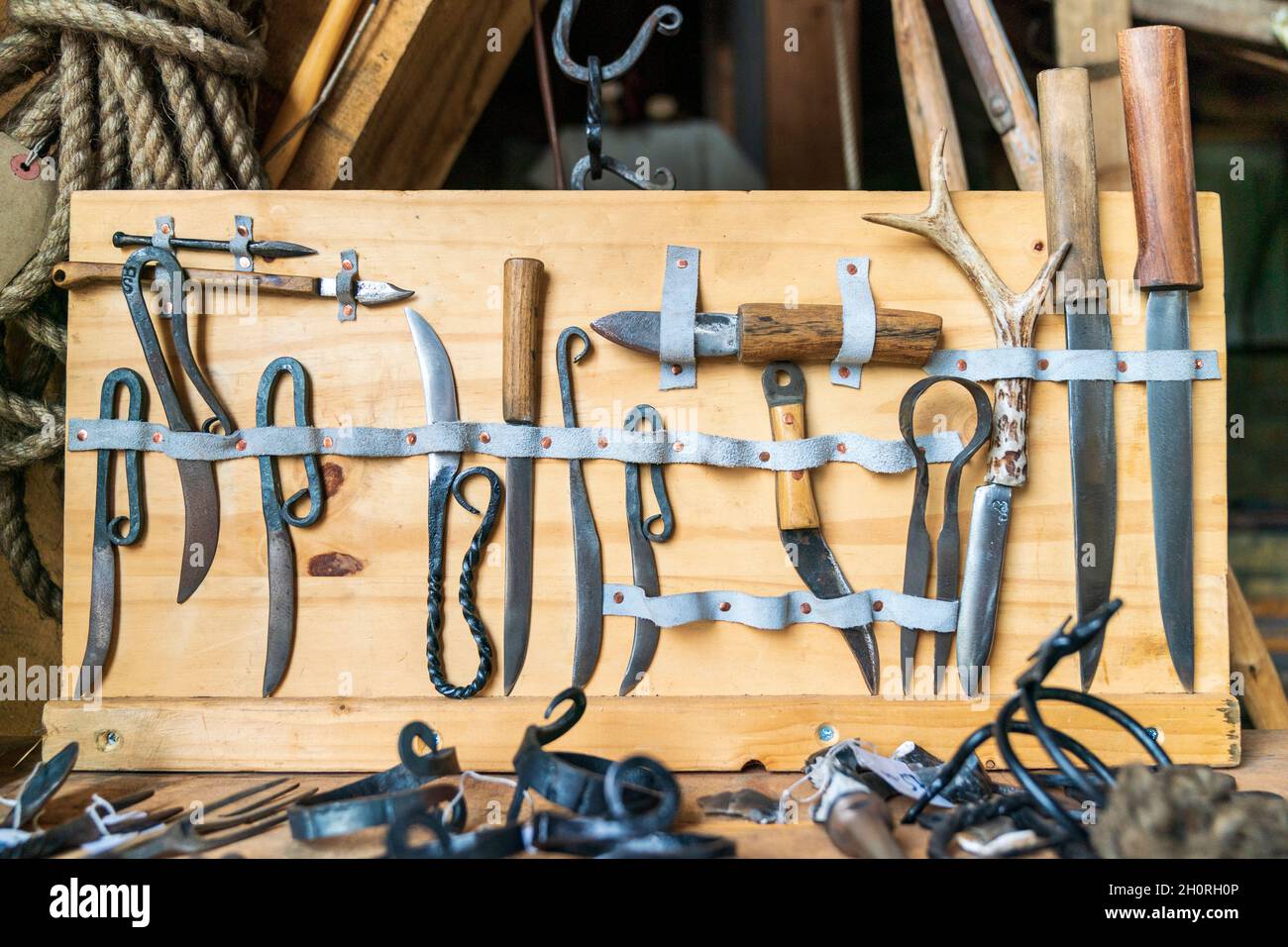 Esposizione di attrezzi di Falegnameria medievali. Vari tipi di coltelli e lame tenuti in posizione da strisce di pelle su pannelli di legno in un'officina di carpentieri. Foto Stock