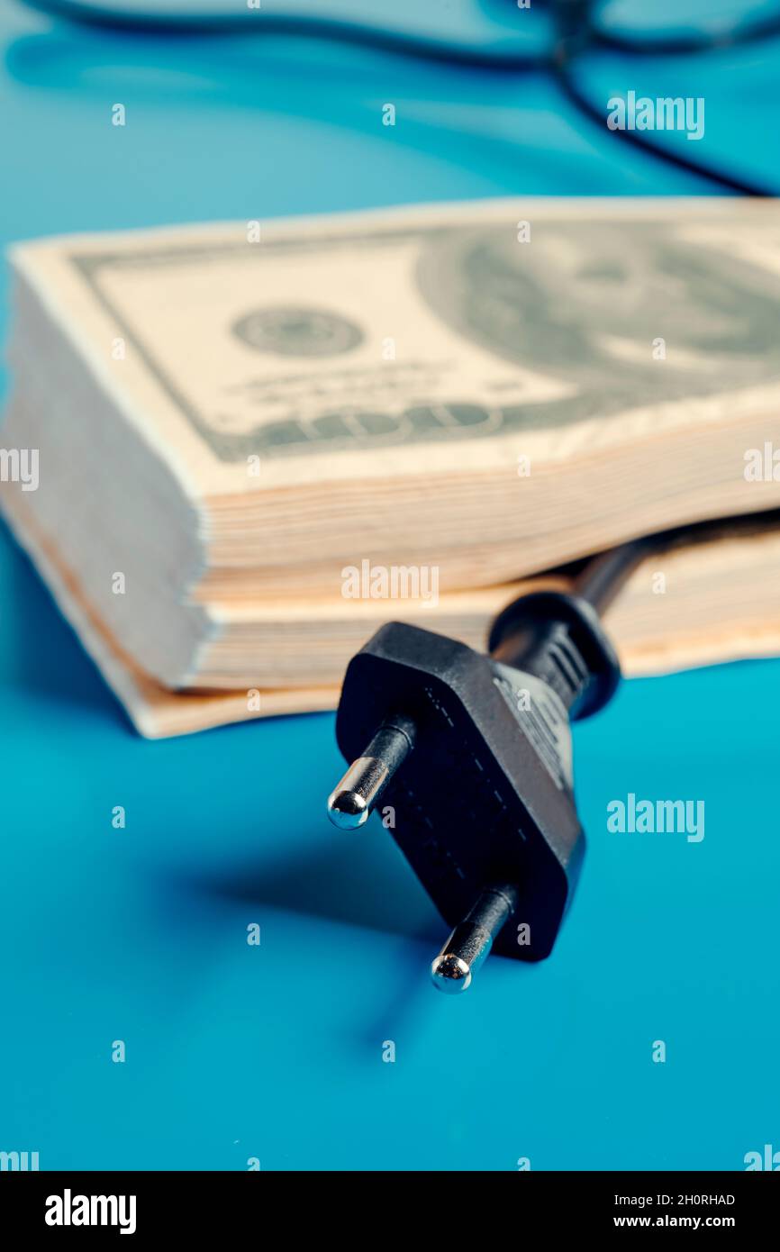 primo piano di un cavo elettrico che emerge da una pila di banconote in dollari, raffigurante l'alto prezzo dell'elettricità Foto Stock