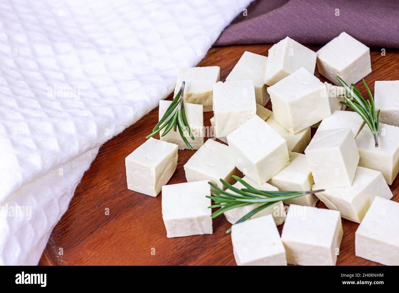 Cubetti di tofu vegetariani biologici crudi con rosmarino fresco su sfondo di legno. Foto Stock