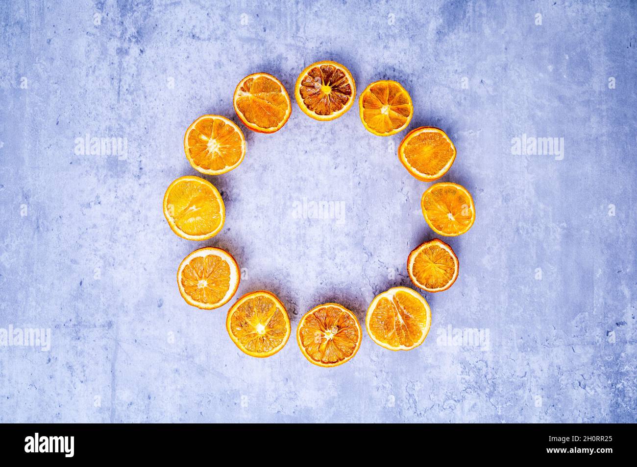 Corona d'Avvento o corona d'Avvento minimalista: Fette di arancio appassite in colori brillanti, disposte in cerchio su sfondo con aspetto concreto. Foto Stock