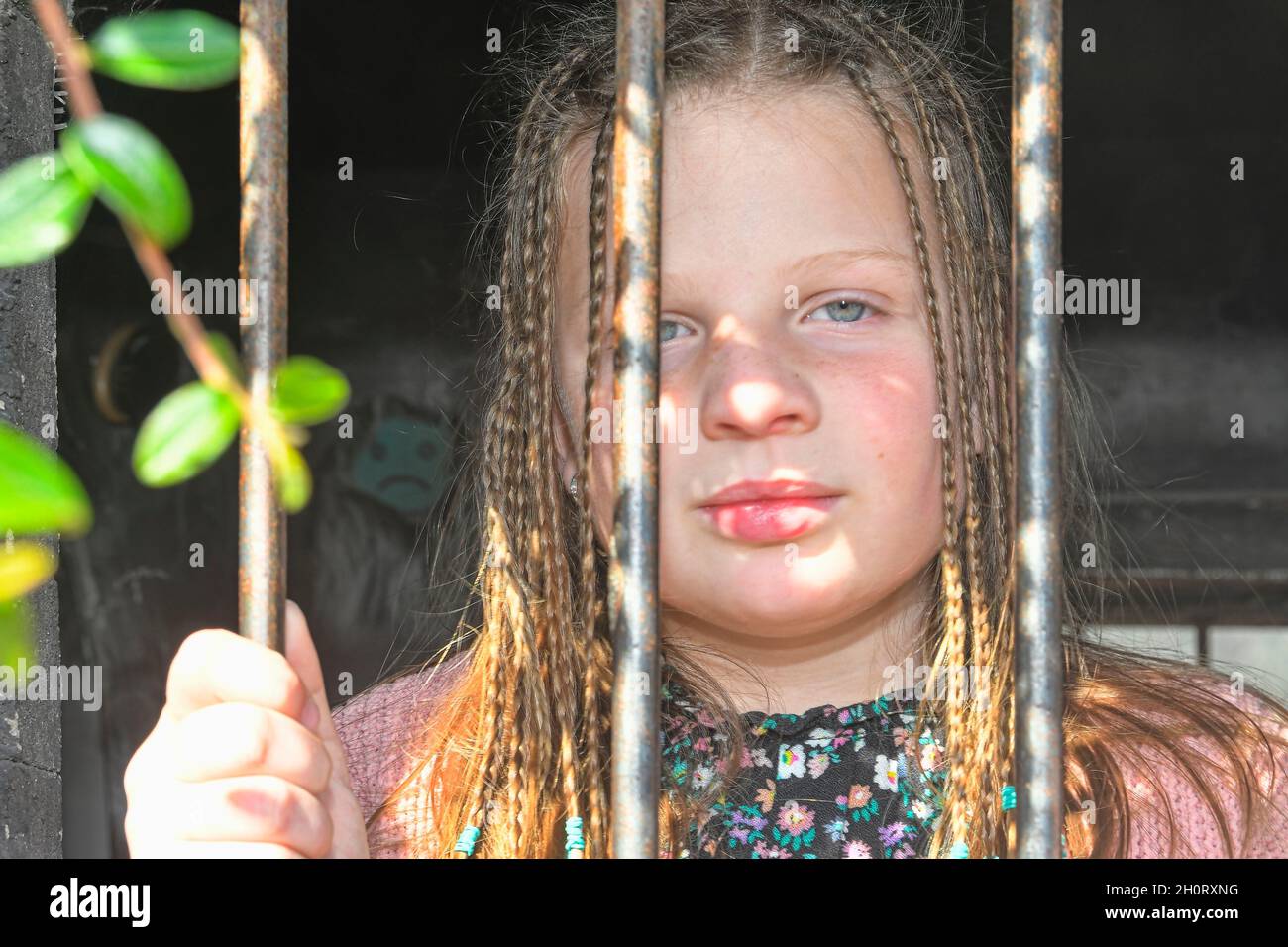 Foto di una bambina che tiene le barre. Ragazza piccola triste dietro le barre di ferro. Bambina dietro le sbarre. Concetto di violenza Foto Stock