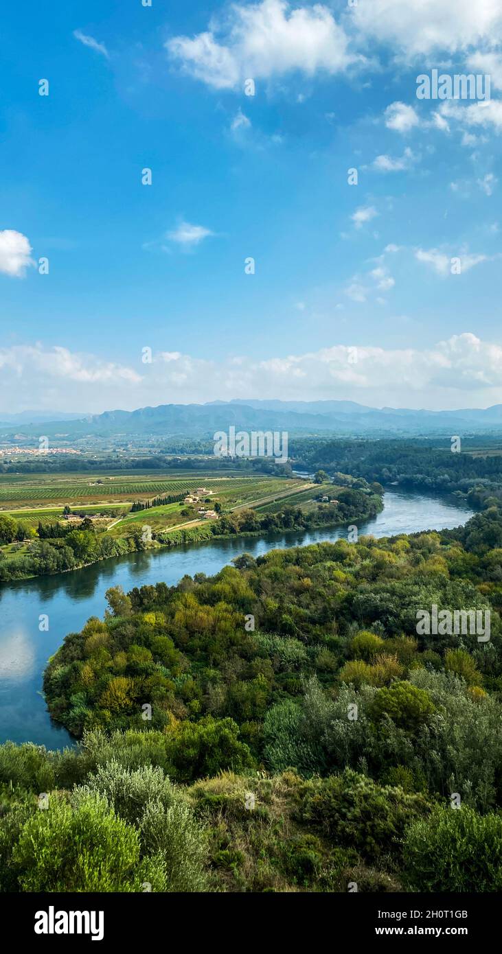 Il fiume Ebro passando per Miravet, in Spagna, con le catene montuose Serra de Cardo ed Els Ports sullo sfondo, in un formato verticale da utilizzare per fo Foto Stock