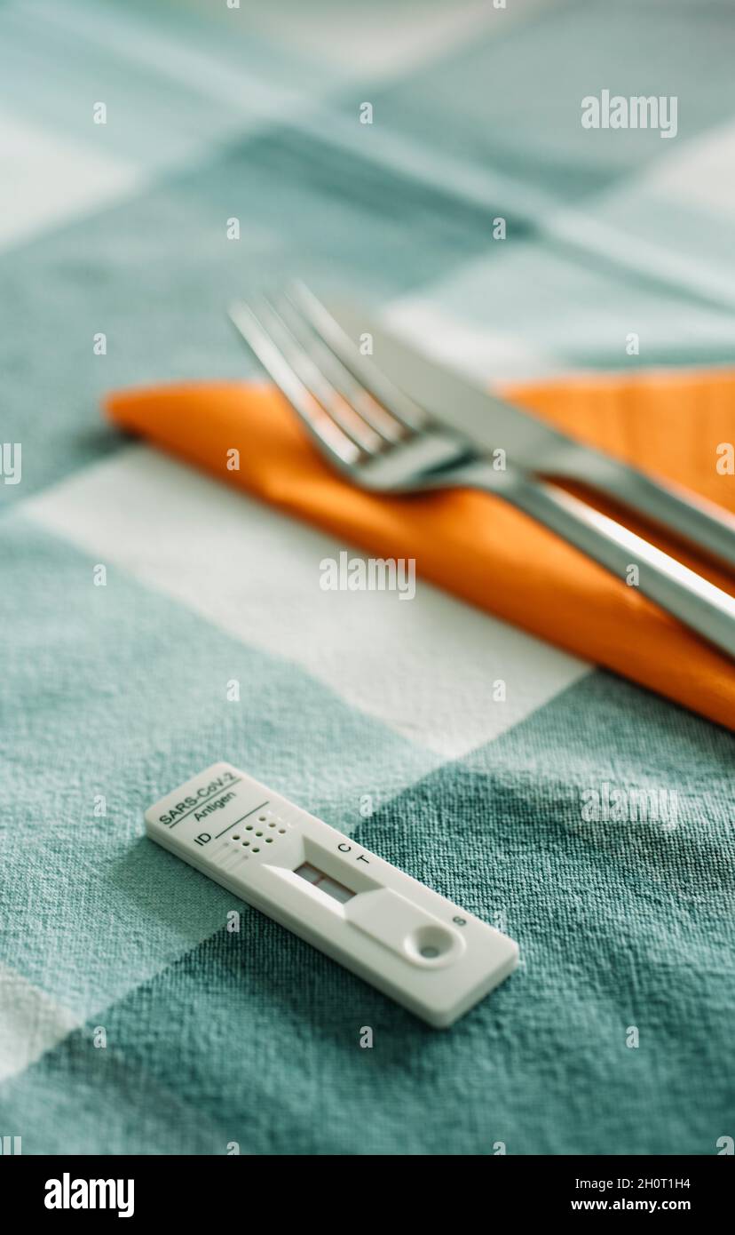 un dispositivo di test diagnostico rapido dell'antigene covid-19 su un tavolo per pranzo, accanto ad una forchetta e un coltello su un tovagliolo di tessuto arancione Foto Stock