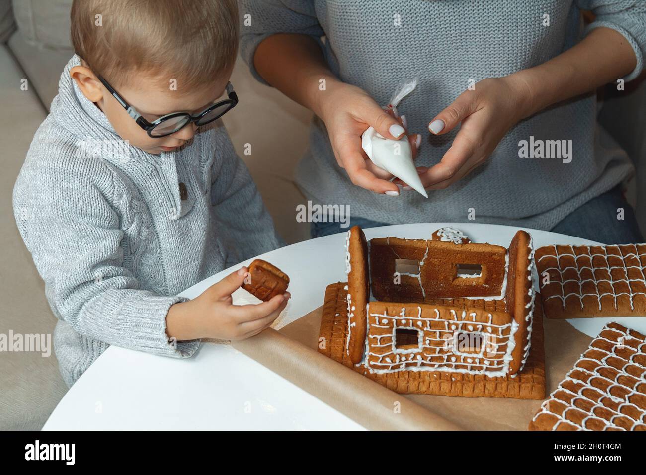 Ragazzino con mamma decorare casa di pan di zenzero di natale insieme Foto Stock