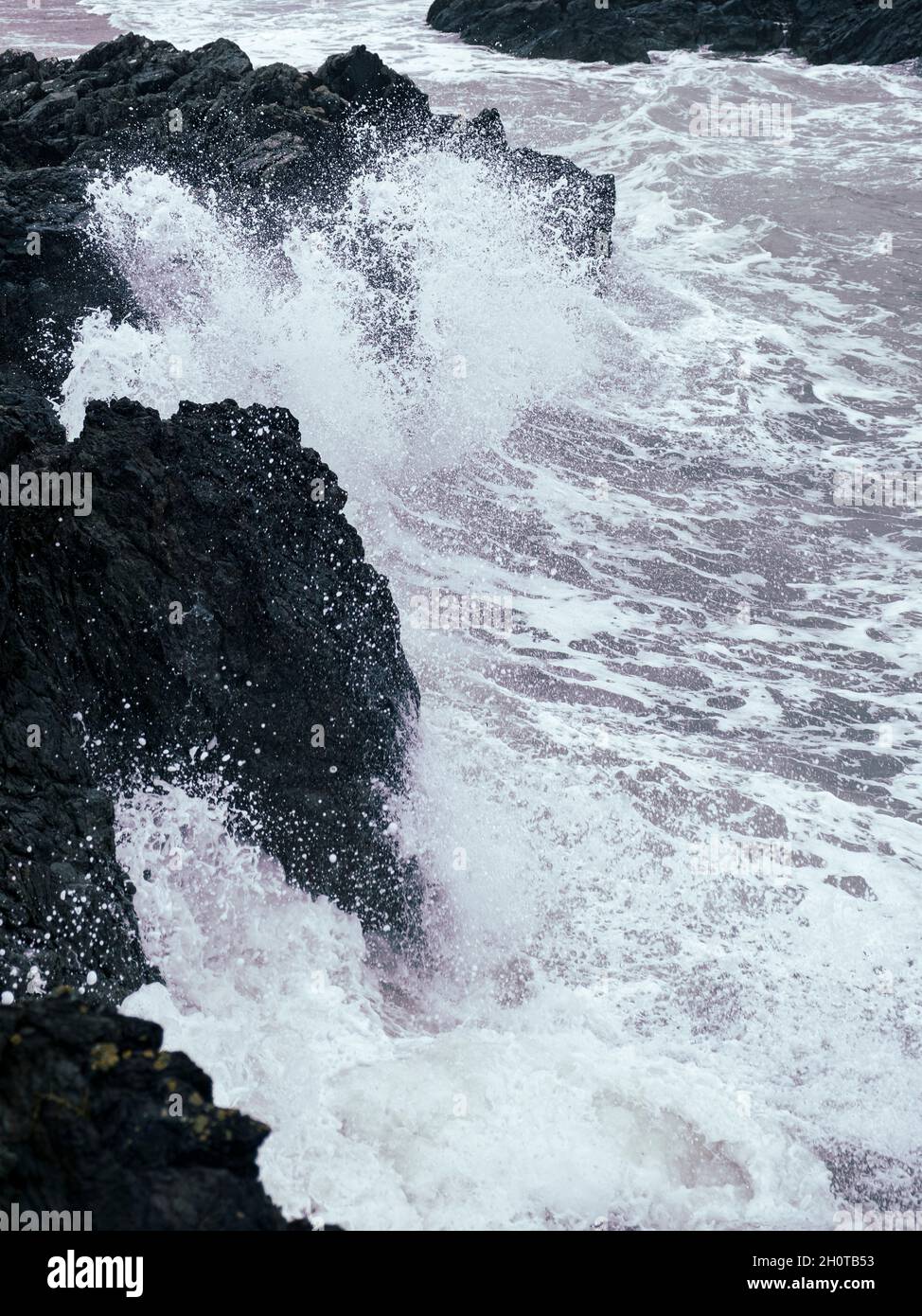 Onde che si infrangono contro rocce al largo della costa di Rhosneigr, Anglesey, Galles del Nord, Regno Unito Foto Stock