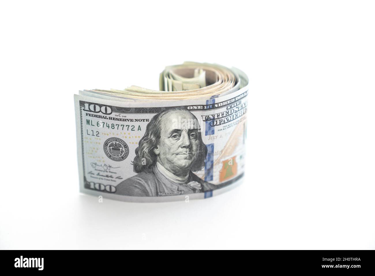 Un'asta arrotolata di soldi con un Benjamin o un dollaro degli Stati Uniti cento fattura sulla parte superiore siede sul bordo e comincia a srotolare o srotolare ed è isolato Foto Stock
